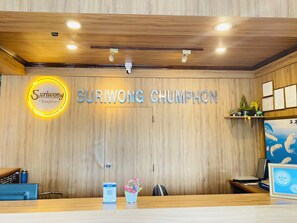 Una recepción con pared de paneles de madera, un letrero que dice 'Surwong Chumphon' y una pequeña estatua de Buda en un estante.