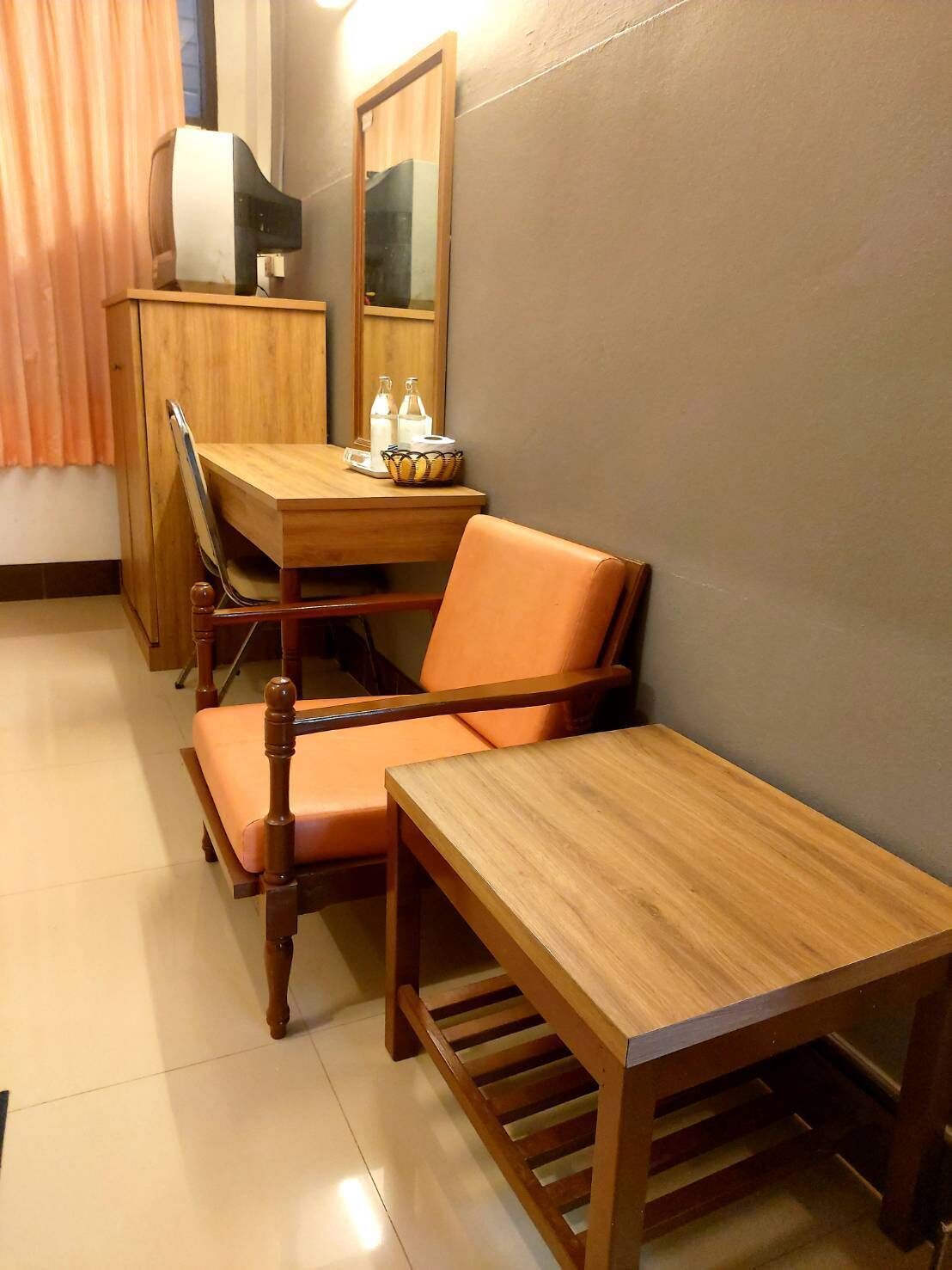 A compact room with a wooden desk, two chairs, a small table, a television on a cabinet, and a mirror on the wall.