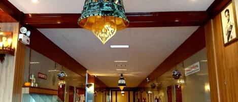 Un pasillo de hotel con una araña central, paneles de madera y plantas en macetas.