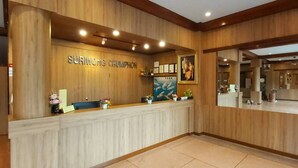 Una zona de recepción con un mostrador de madera, un cartel que dice "SURIWONG CHUMPHON" y una gran foto enmarcada sobre el mostrador.