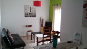 A living room with a sofa, a dining table, a TV, and a painting of the Eiffel Tower. - Elenapa Holiday Apartments (Ayia Napa)