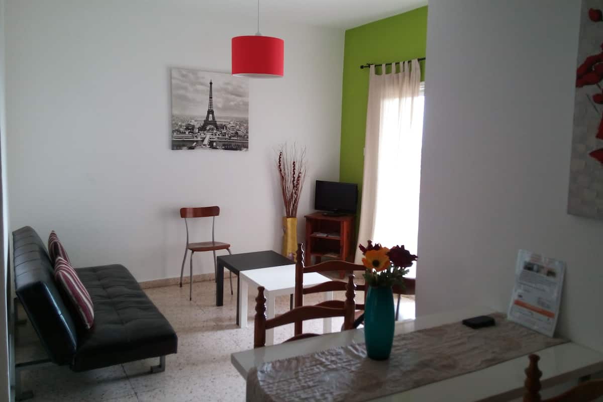 A living room with a sofa, a dining table, a TV, and a painting of the Eiffel Tower.