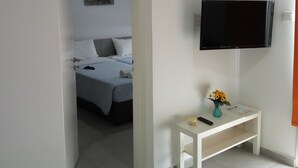 A hotel room with a bed, a TV mounted on the wall, a small table with a vase of flowers, and a painting on the wall. - Elenapa Holiday Apartments (Ayia Napa)