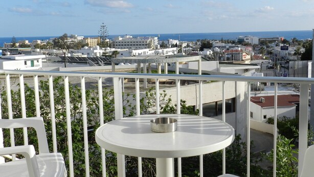 A balcony with a round table and chairs, overlooking a coastal cityscape with buildings and a clear sky. - Elenapa Holiday Apartments (Ayia Napa)
