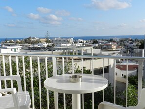 Un balcón con una mesa redonda y sillas, con vistas a una ciudad costera con edificios y cielo despejado.