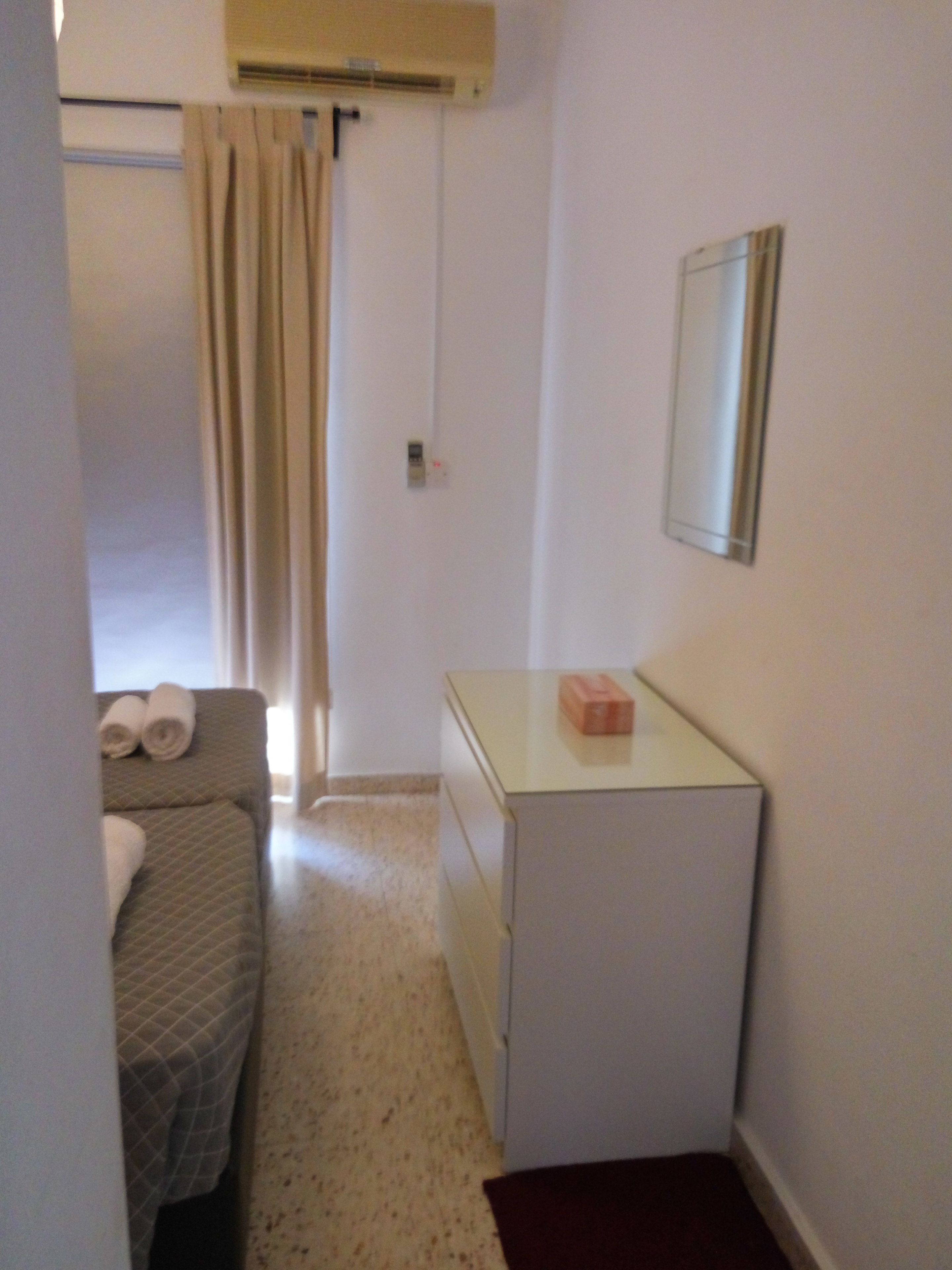 A small, compact room with a bed, a desk, and a mirror.