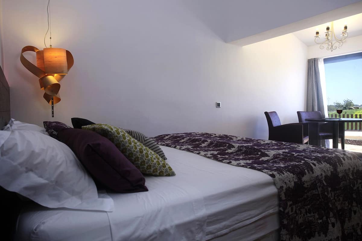 A hotel room with a bed, pillows, a desk, and a chair.