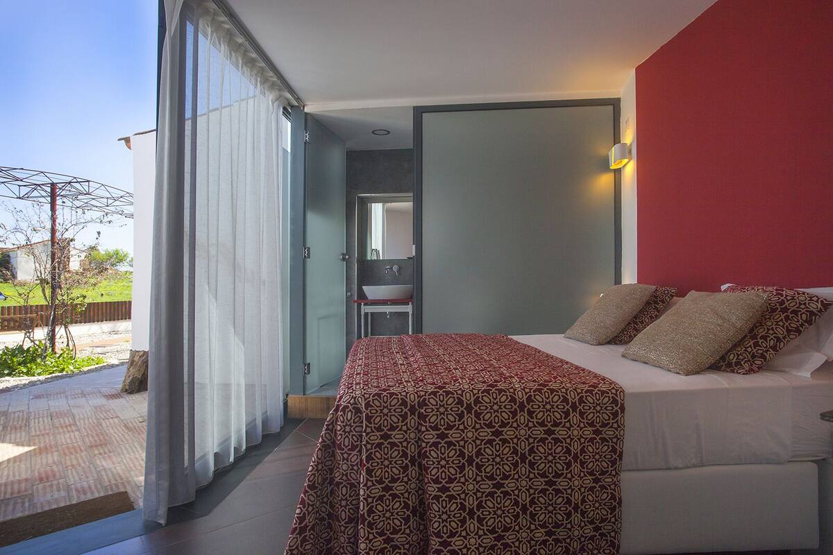 A bedroom with a bed, a bedside table, a mirror, and a window with curtains.
