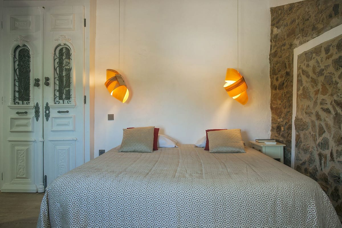 A bedroom with a large bed, two wall-mounted lamps, a stone accent wall, and a door with decorative ironwork.