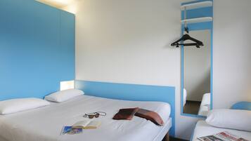 Ett hotellrum med en säng, ett sängbord, en spegel och en klädstång.