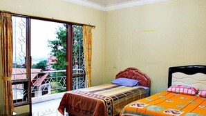 Une chambre avec deux lits, un balcon donnant sur des immeubles et une fenêtre avec des barreaux en métal.
