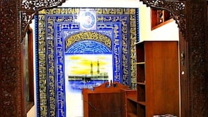 Une pièce avec un mur orné d’un motif bleu et doré, une porte en bois et un petit bureau en bois avec une chaise.