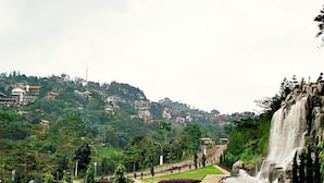 Un parc doté d’une cascade, de jardins aménagés et d’une colline parsemée de bâtiments.