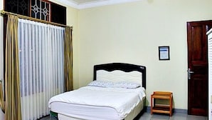 Une chambre à coucher avec un lit, des rideaux, une porte en bois et un petit tabouret en bois.