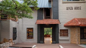 Un edificio con el letrero 'River House', que cuenta con una terraza de madera que conduce a una entrada cubierta, paredes de piedra y vistas al exterior.