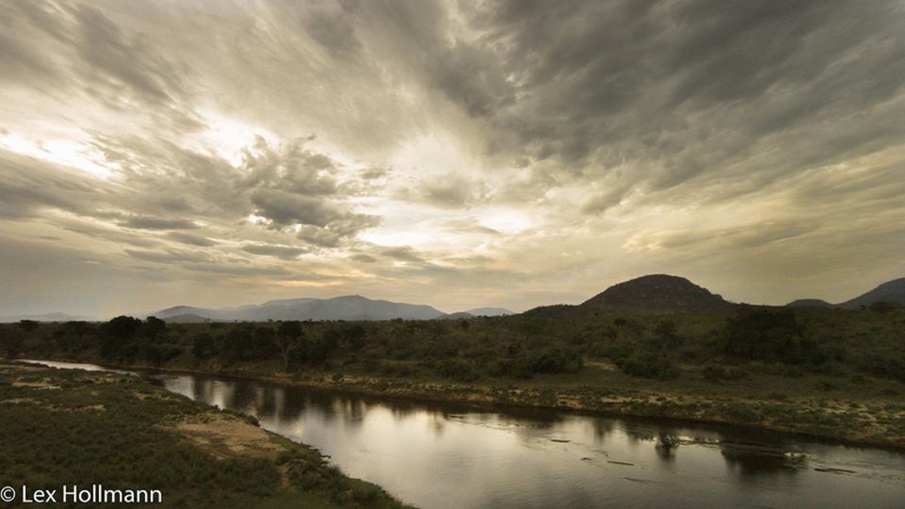 Rivierlandschap met een berg op de achtergrond en een bewolkte lucht.