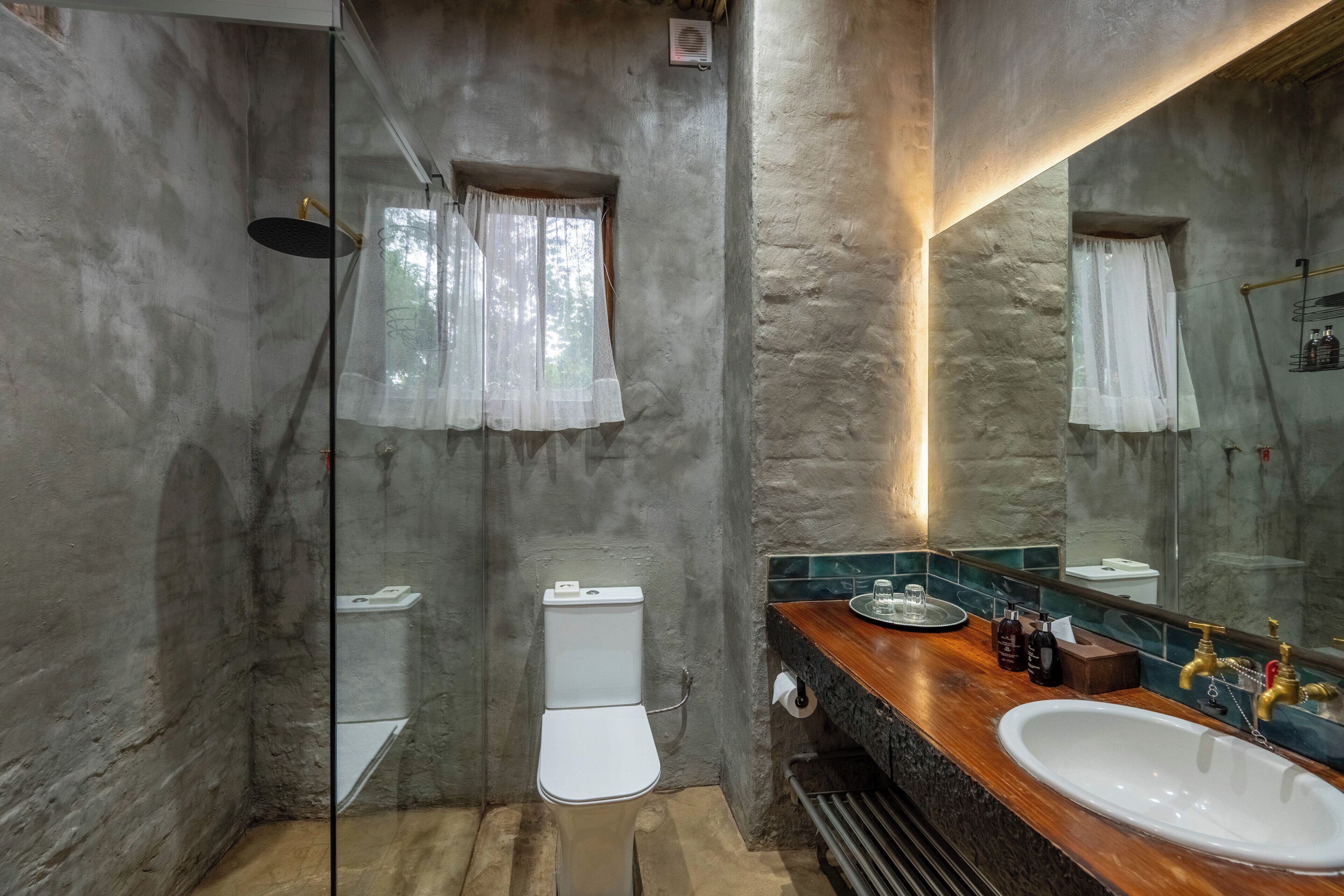 Une salle de bain avec un mur en pierre, un meuble-lavabo en bois, un lavabo blanc et une cabine de douche en verre.