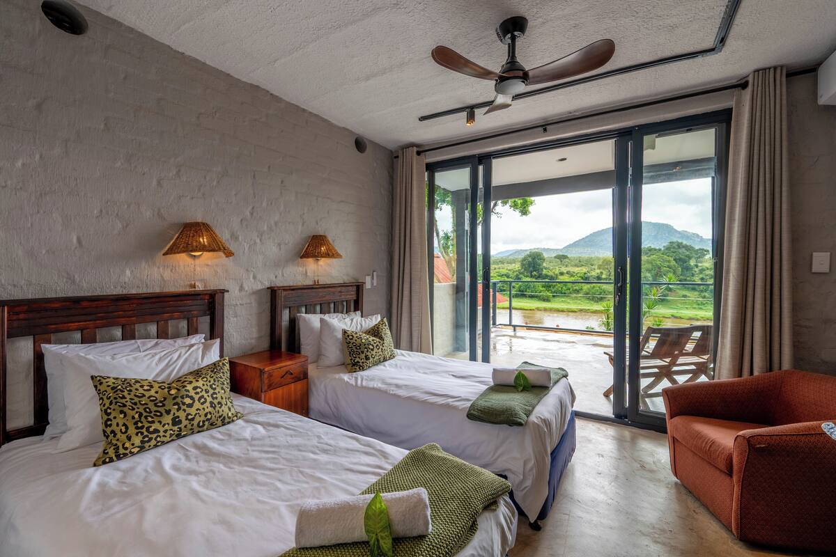 A hotel room with two beds, a balcony with a view, a ceiling fan, and a red chair.