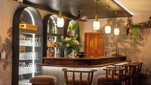Zona de bar con sillas de madera, barra y estanterías con botellas.