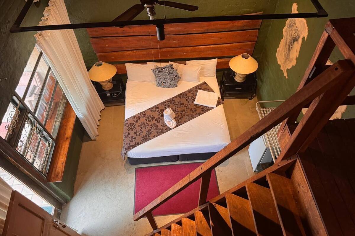 A bedroom with a bed, two bedside lamps, a red rug, and a wooden staircase.