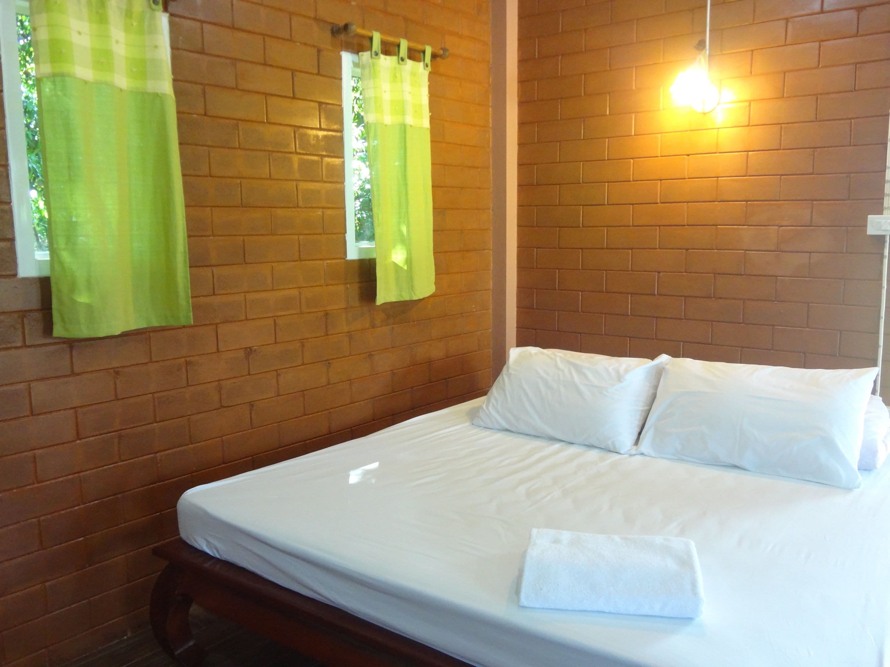 Una cama bien tendida en una habitación con paredes de ladrillo y una lámpara colgante.