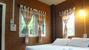 Una habitación de hotel con pared de ladrillo, cama con ropa blanca y cortinas en las ventanas.