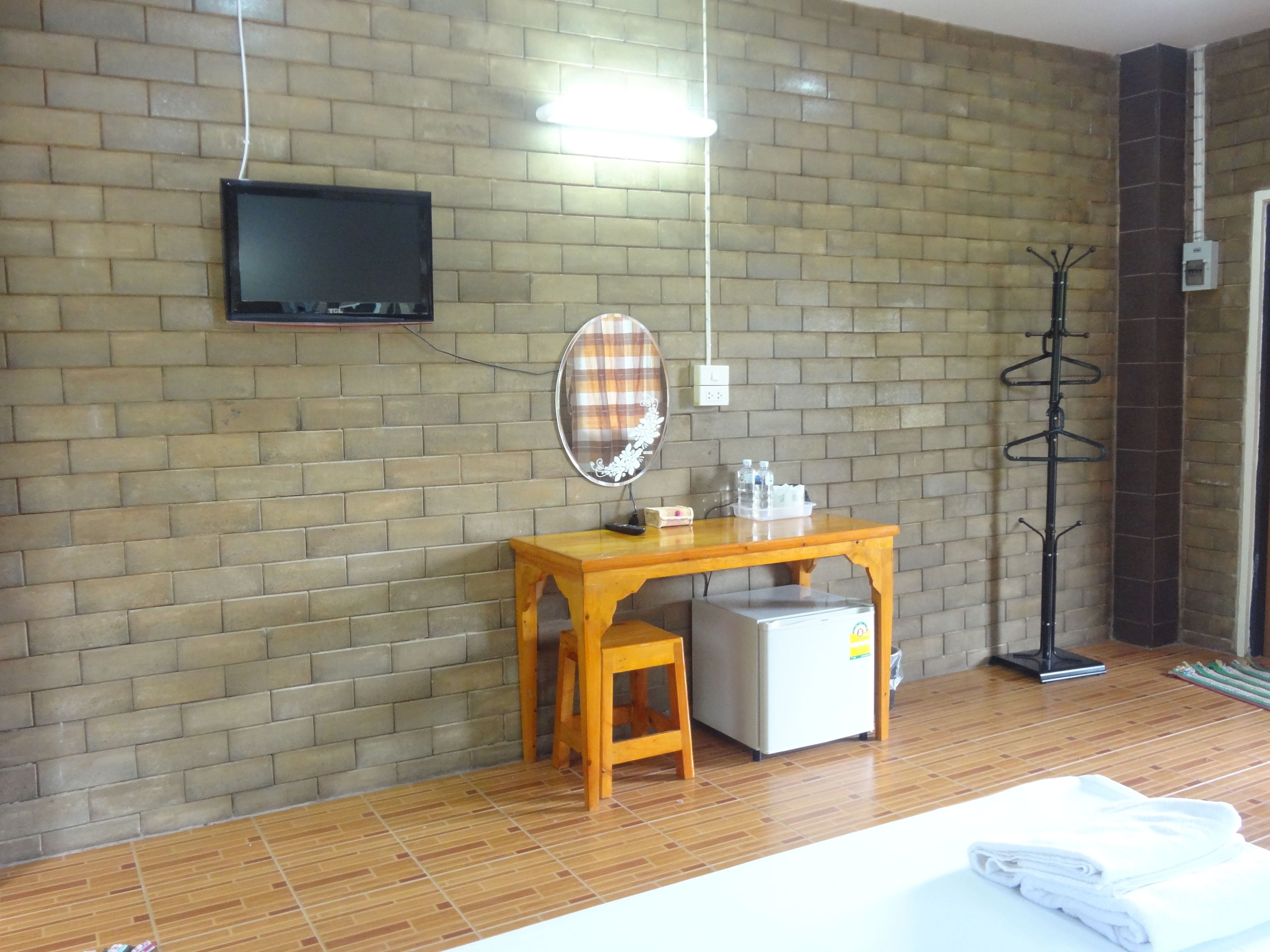 Una habitación de hotel con pared de ladrillo, una mesa de madera con espejo, un televisor montado en la pared, un perchero y una cama con toallas dobladas.
