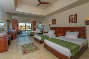 A hotel room with two beds, a desk, a chair, a television, and a view of the outside. - Bliss Laguna Beach Resort (Marsa Alam)