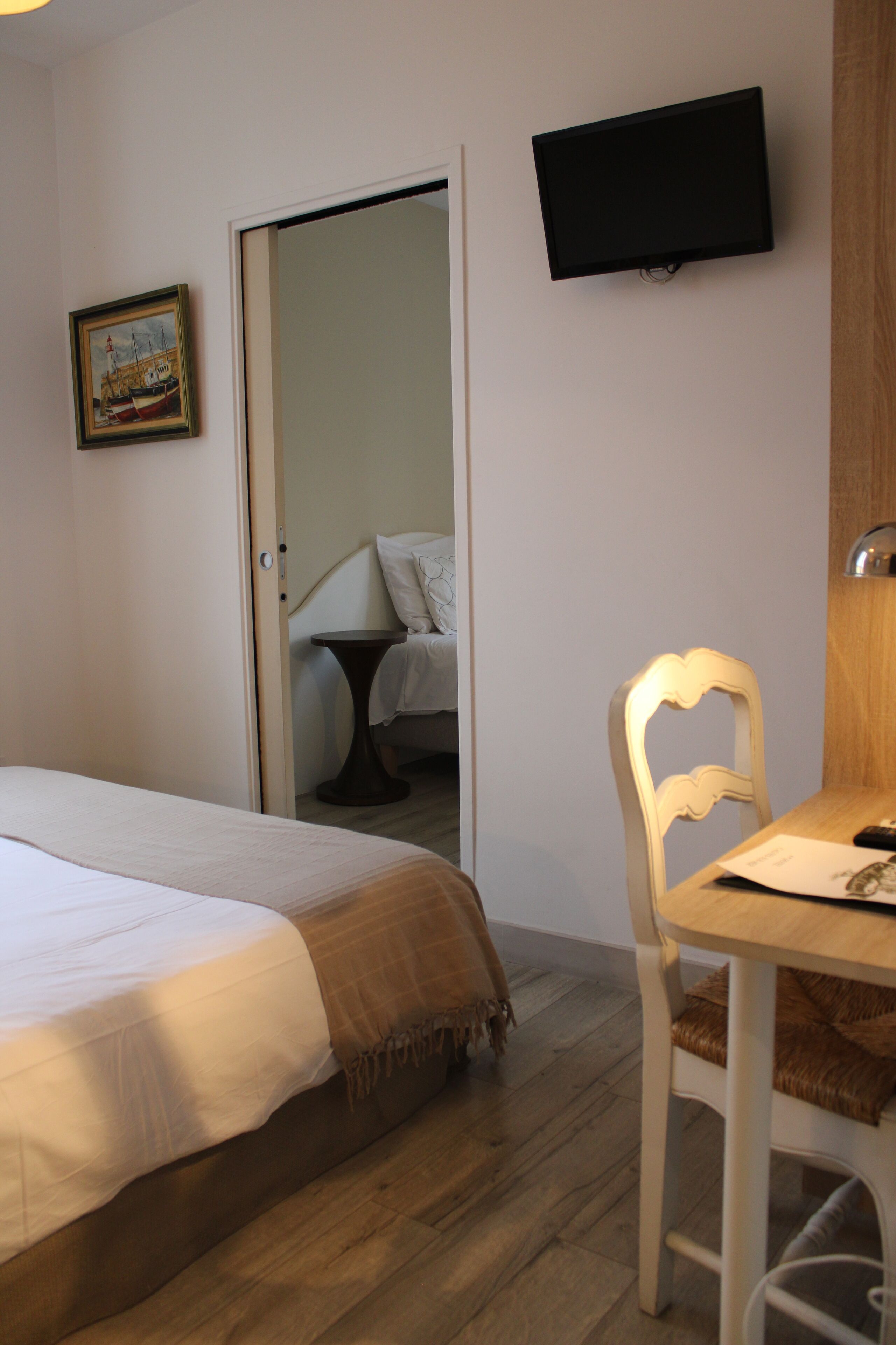 A bedroom with a bed, a desk with a chair, a television mounted on the wall, and a door leading to another room.