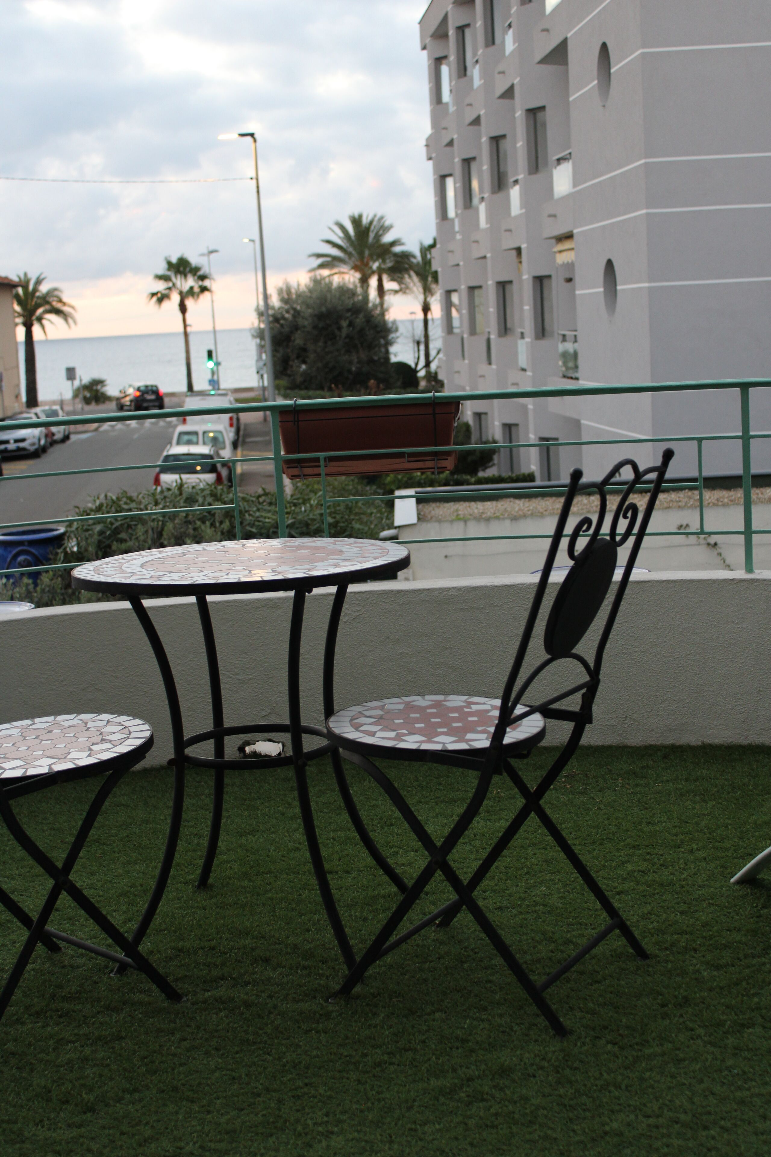 A terrace with two round tables and a chair, overlooking a road with cars and a building in the background.