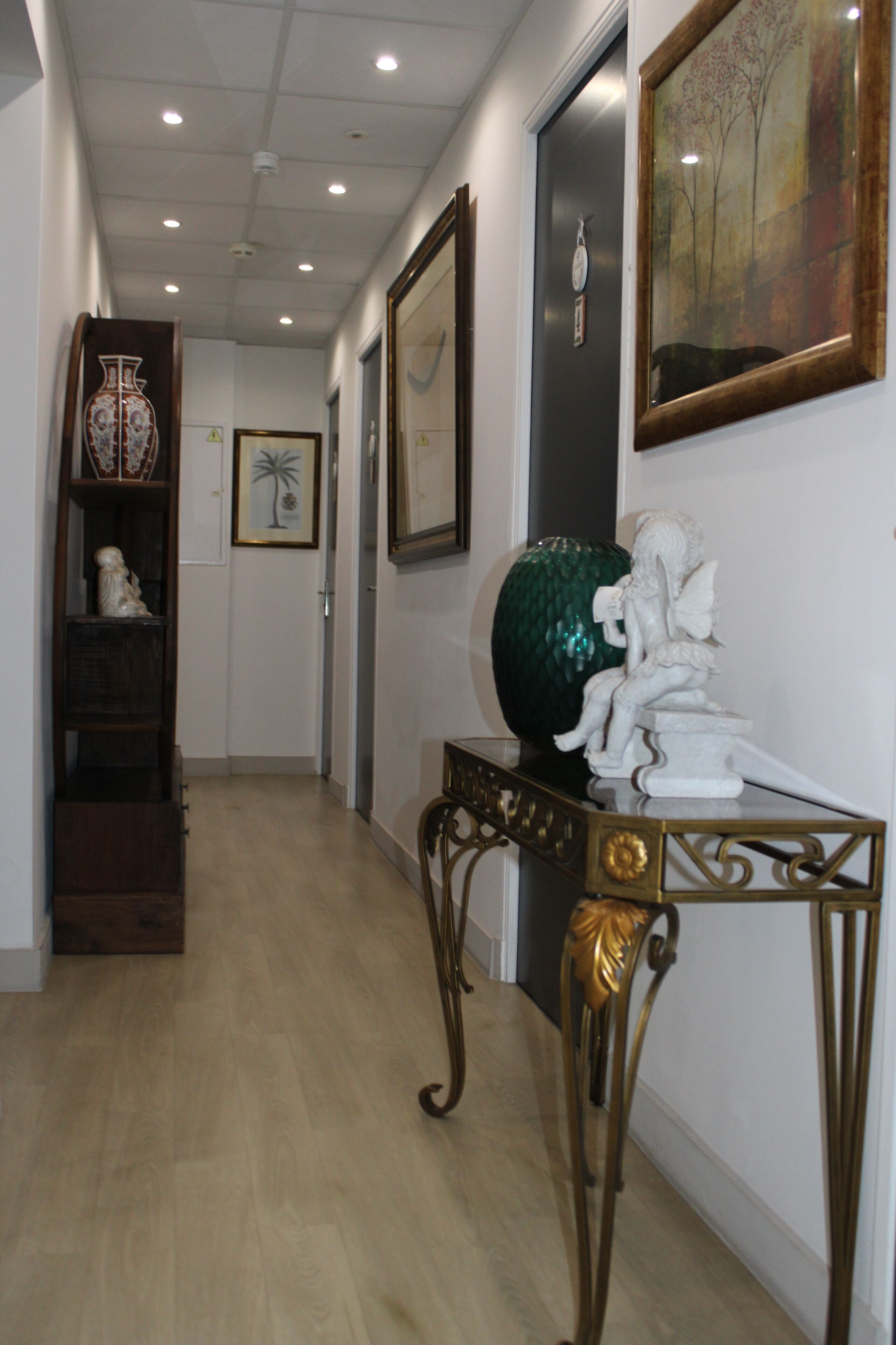 Un pasillo con suelo de madera, una mesa decorativa con un jarrón verde y una estatua.