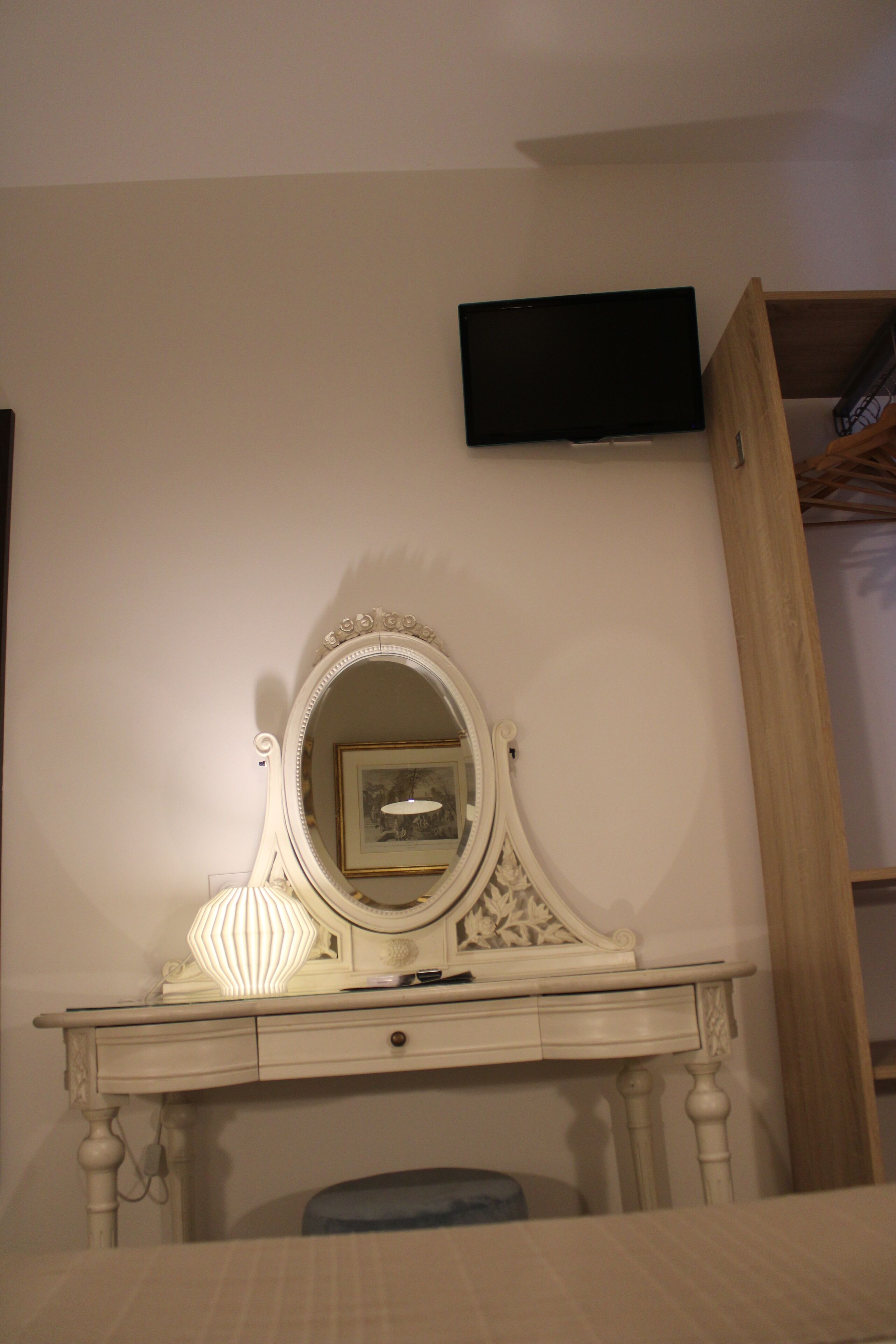 Una habitación con una mesa de tocador, un espejo, un televisor montado en la pared y un armario de madera.