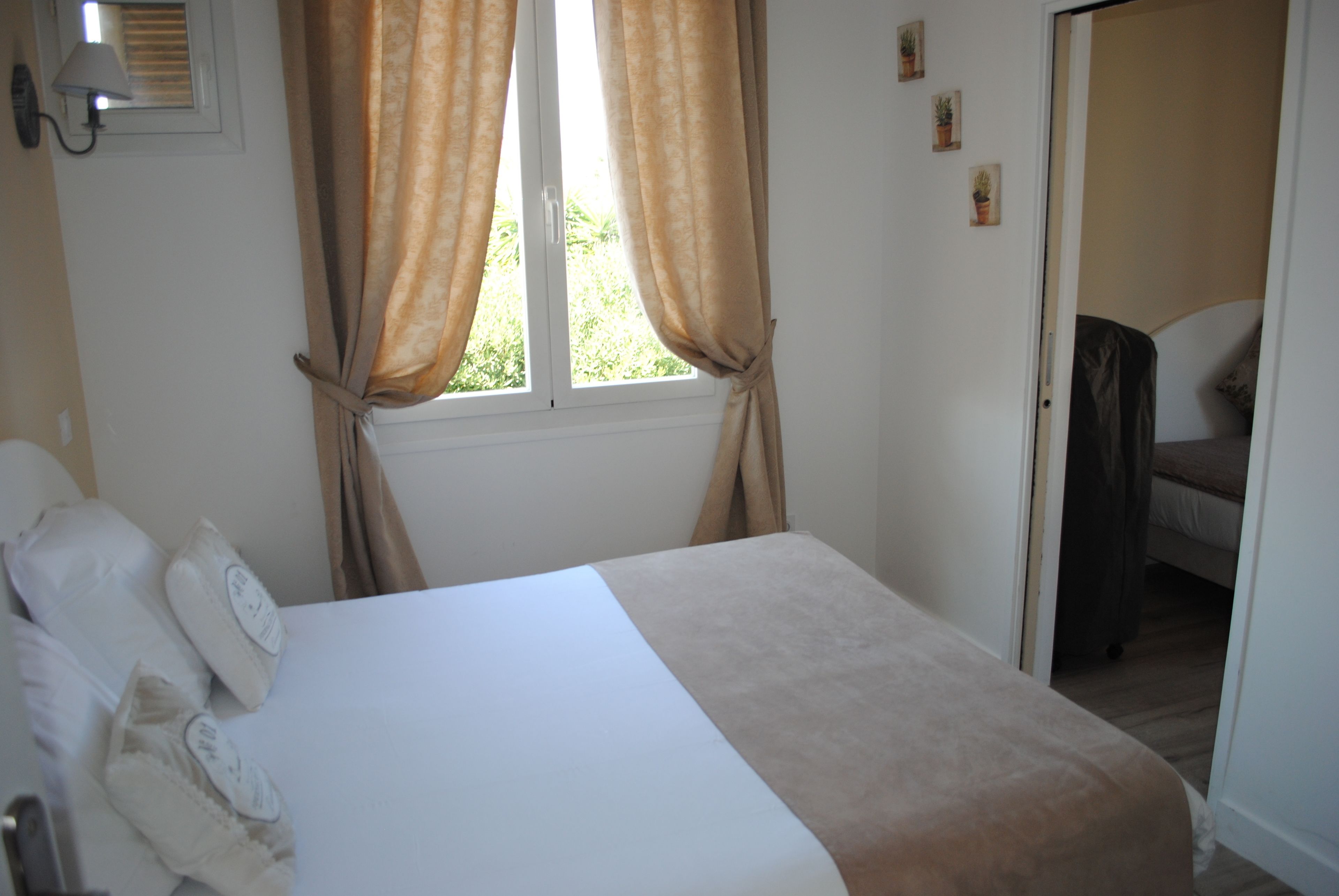A bedroom with a bed, curtains, a window, and a door leading to another room.