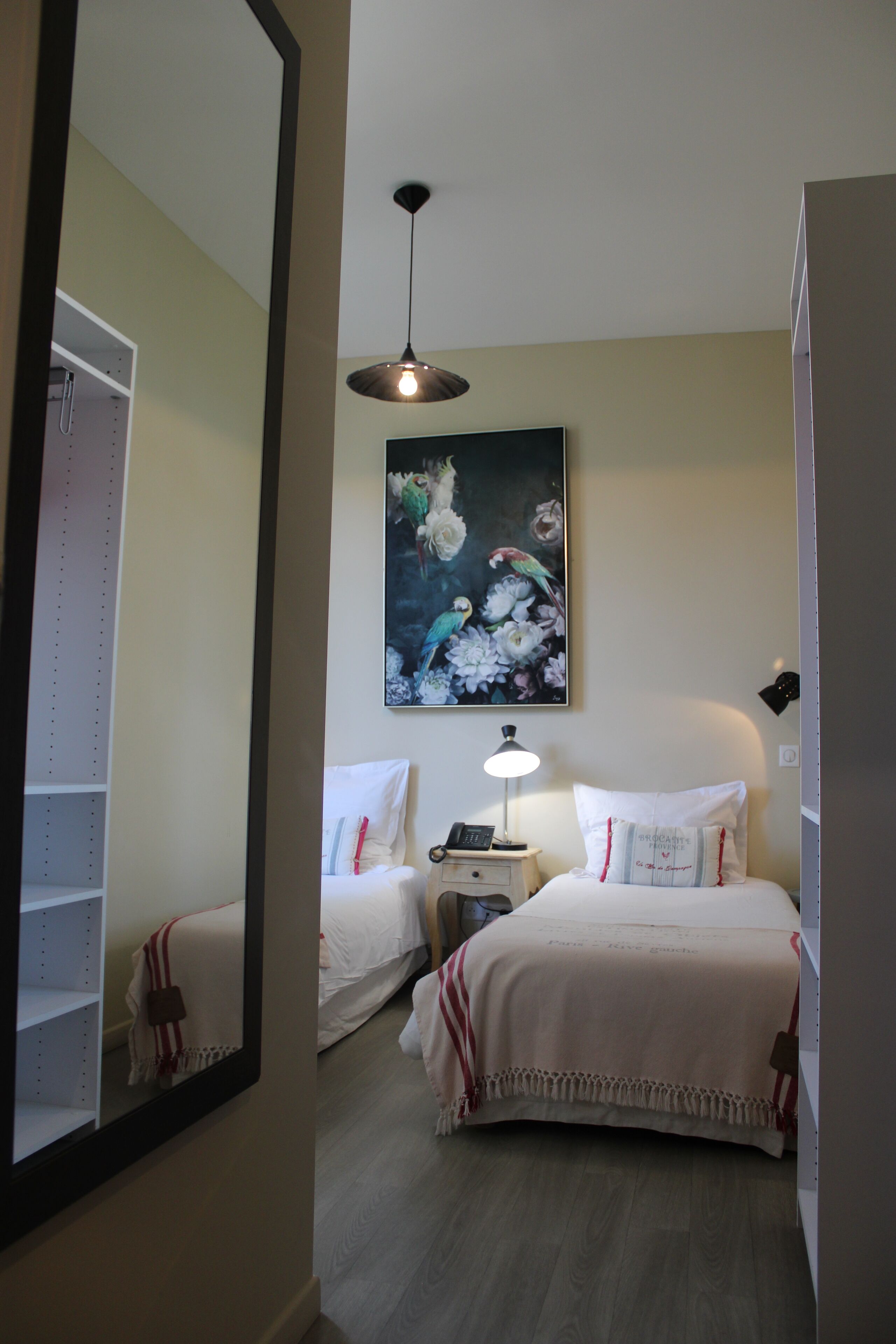 A bedroom with two beds, a nightstand with a lamp, a painting on the wall, and a wardrobe.