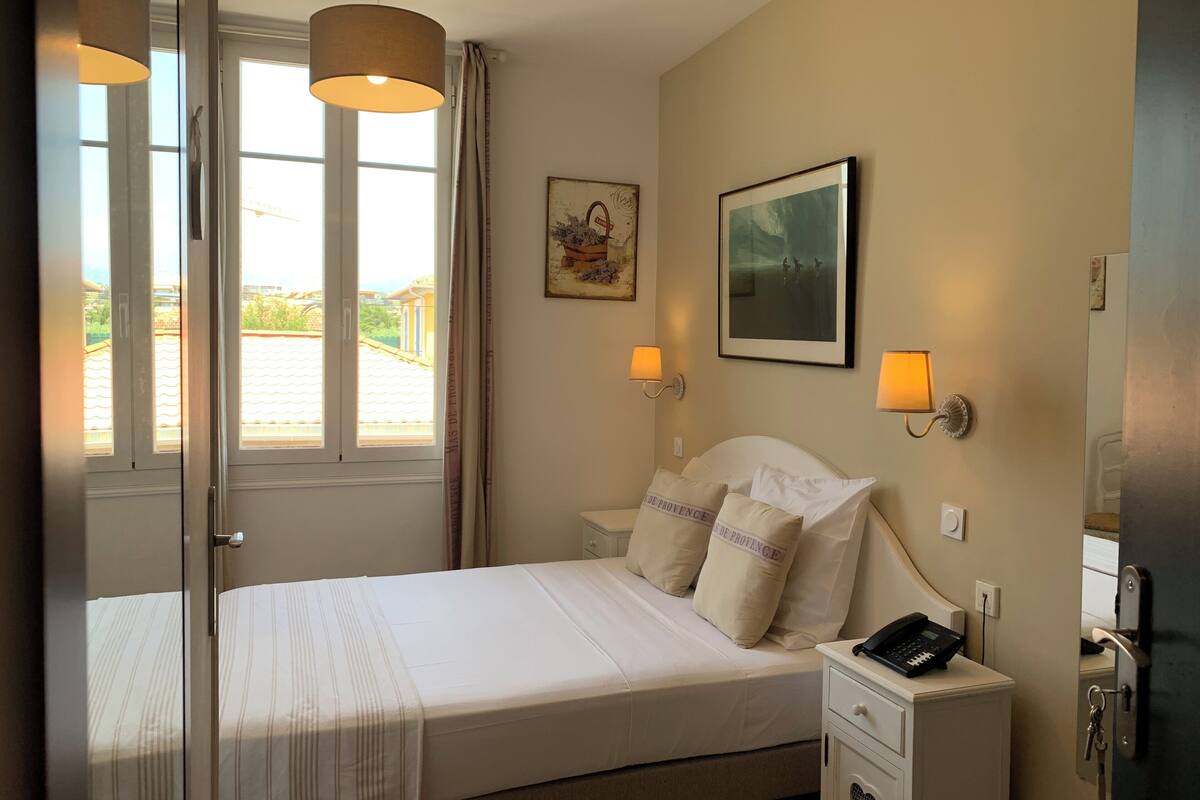 Une chambre d’hôtel avec un lit, des lampes de chevet, un téléphone et une fenêtre avec des rideaux.