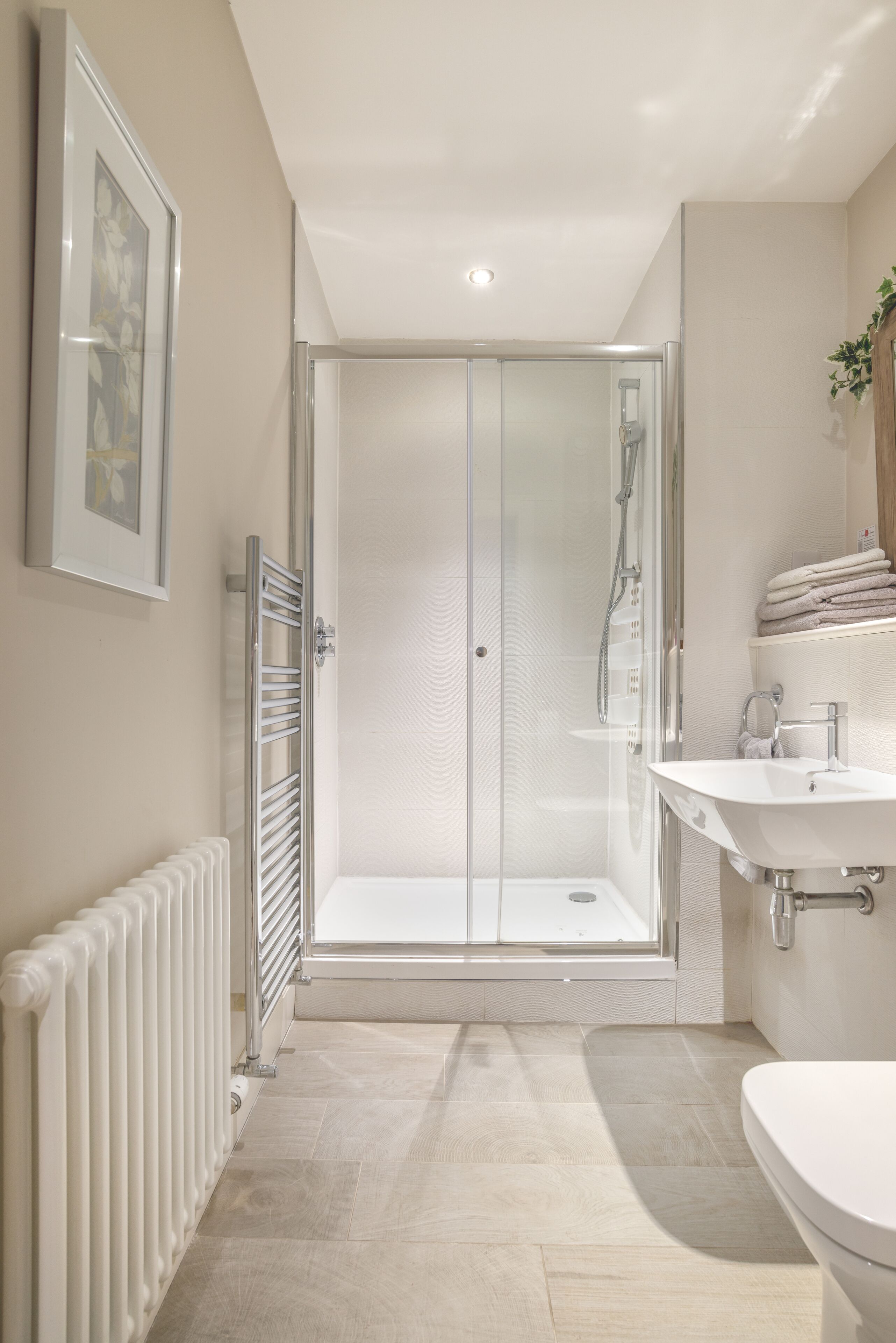 A modern bathroom with a glass-enclosed shower, a white sink, and a radiator.