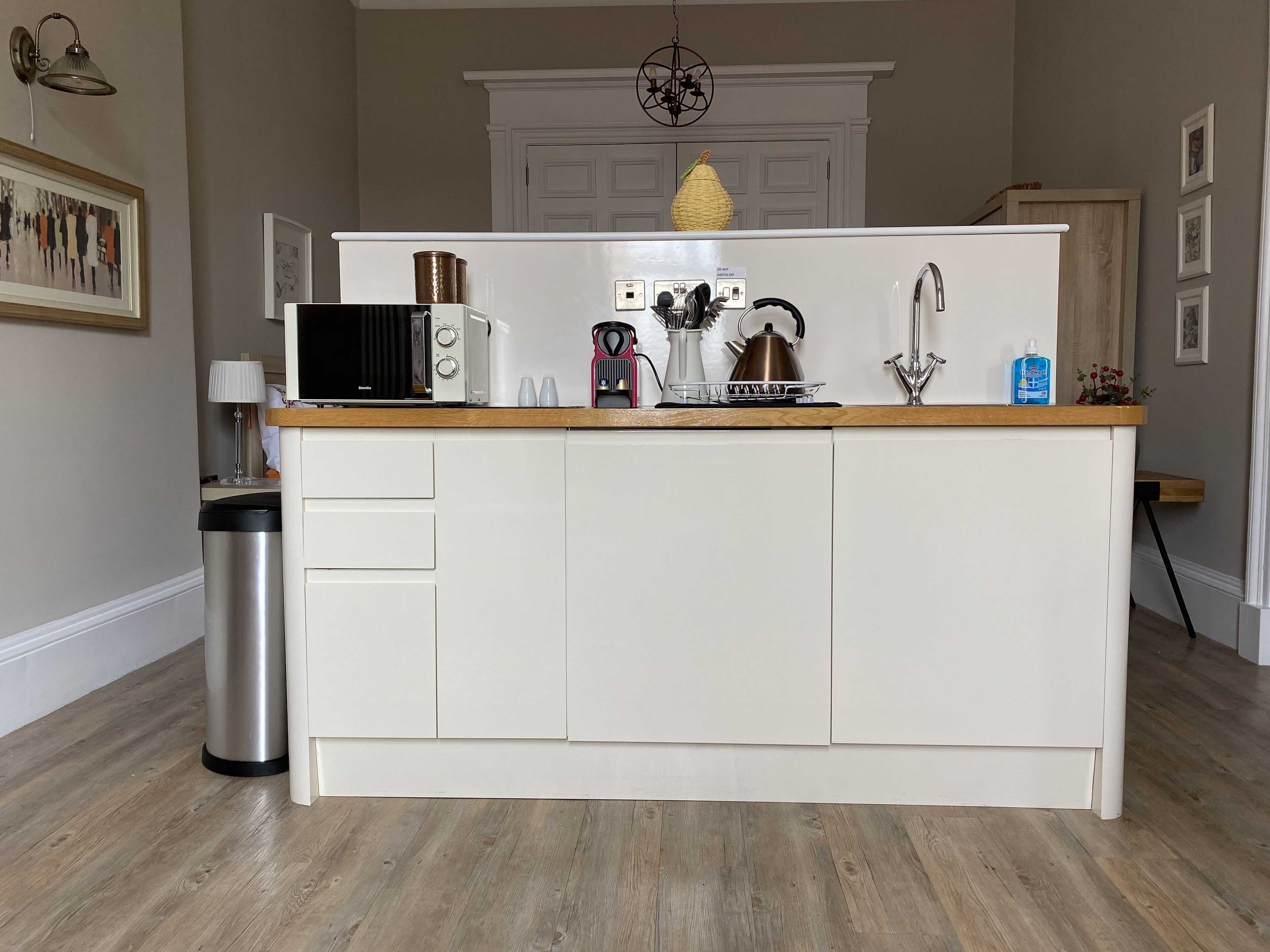 Een keuken met een centraal eiland, witte kasten, een roestvrijstalen prullenbak en een houten aanrecht.