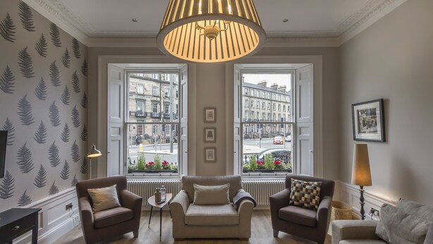 Een woonkamer met twee banken, een salontafel en een lamp. Twee ramen bieden uitzicht over de stad.
