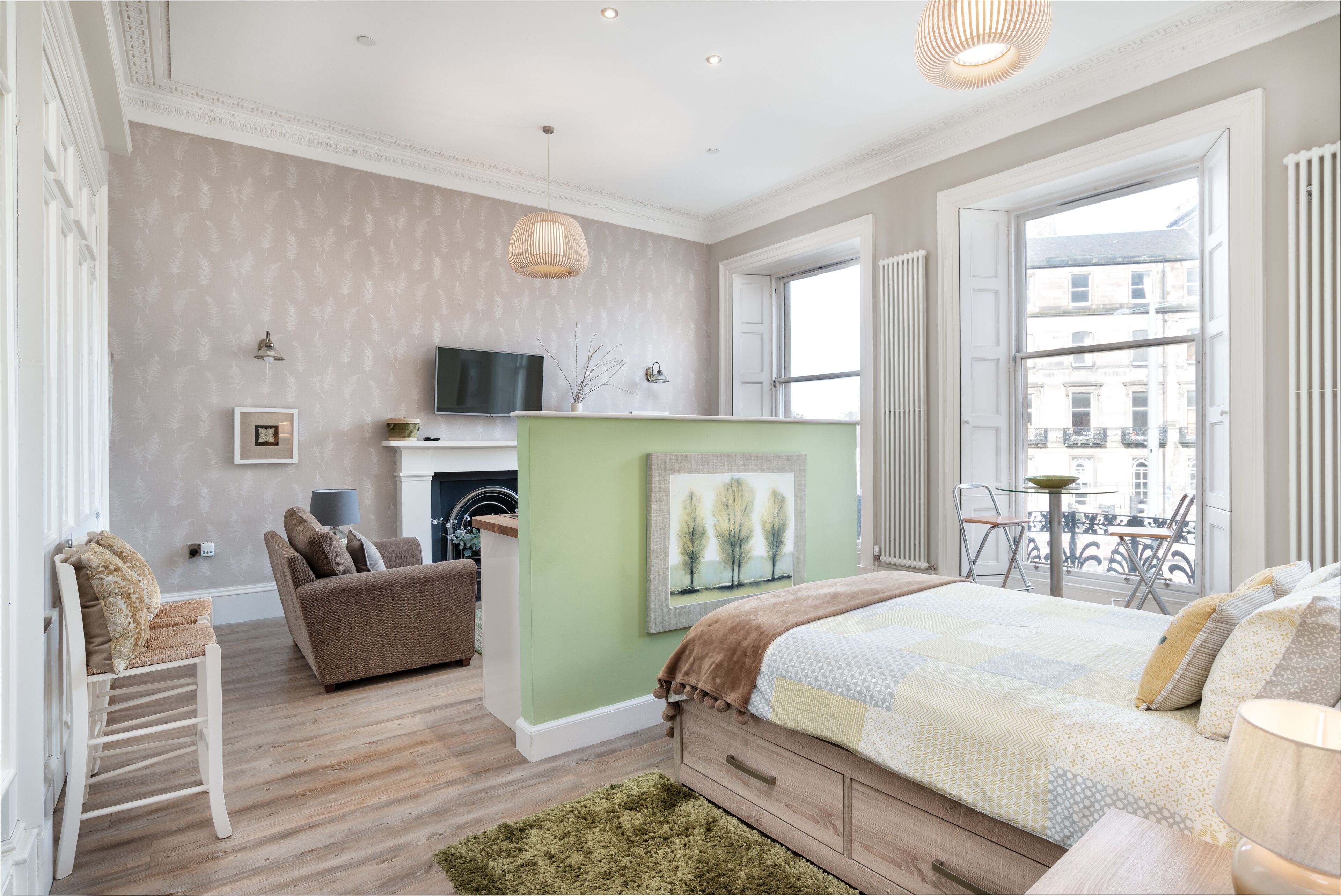 Un dormitorio con cama, sofá, silla, televisión y ventana con vistas a edificios.