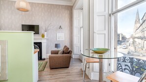 Een woonkamer met een bank, een glazen tafel met een schaal, een televisie en een open haard.