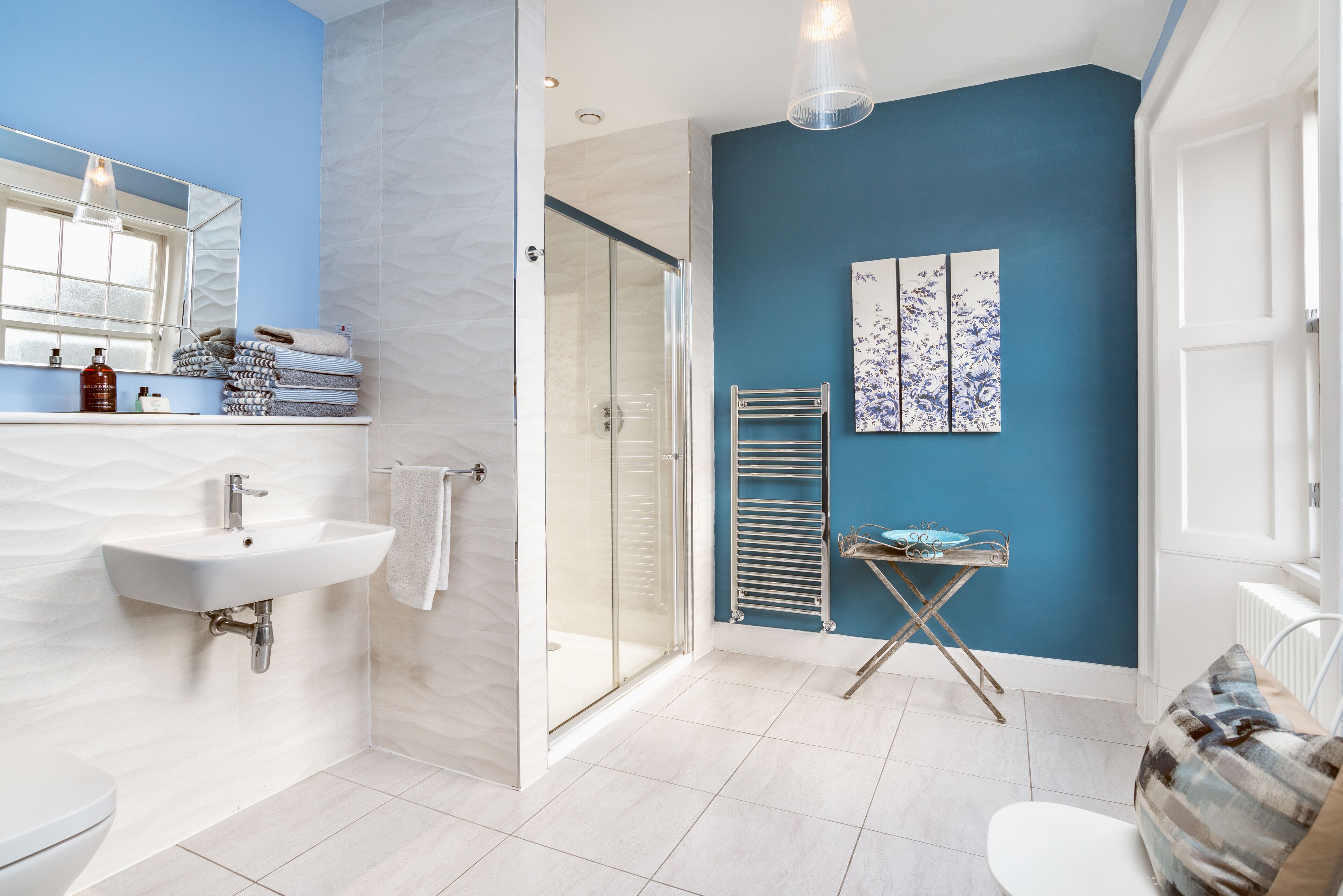 Un baño moderno con un lavamanos blanco, mampara de ducha de cristal y una pared de acento azul.