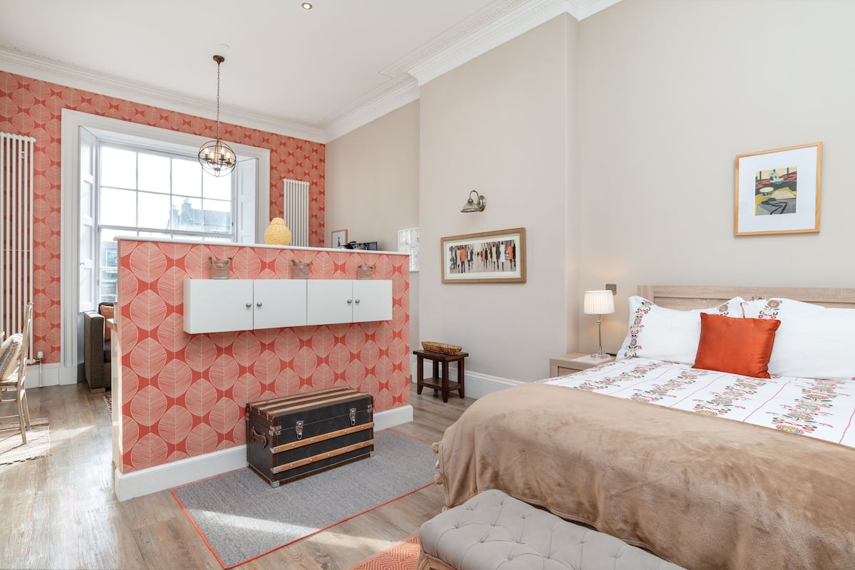 A bedroom with a bed, a dresser, a suitcase, and a window.