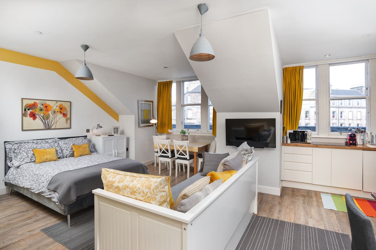 A modern apartment with a loft-style bedroom, a dining area, and a kitchenette.