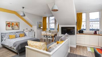 A modern apartment with a loft-style bedroom, a dining area, and a kitchenette.