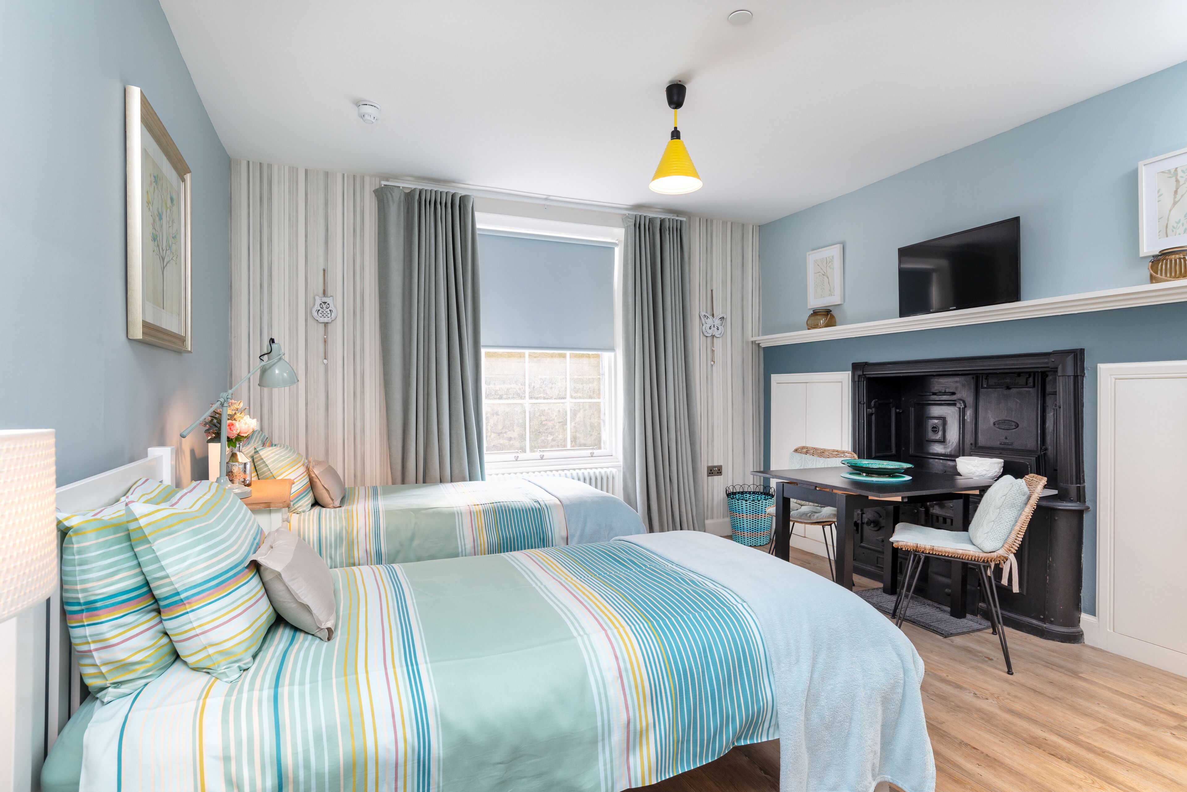A bedroom with two beds, a desk, a chair, a fireplace, and a television.