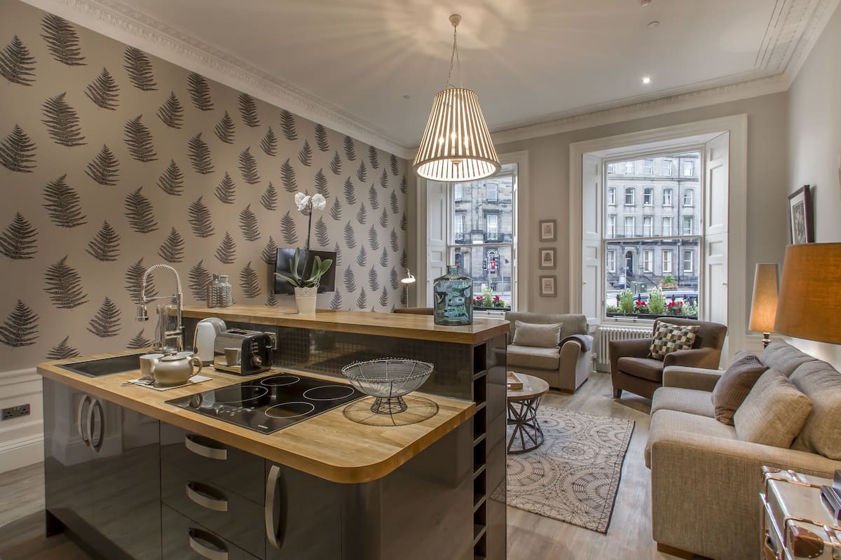 A modern kitchen with a central island, a dining area with a sofa, and a view of the city through large windows.