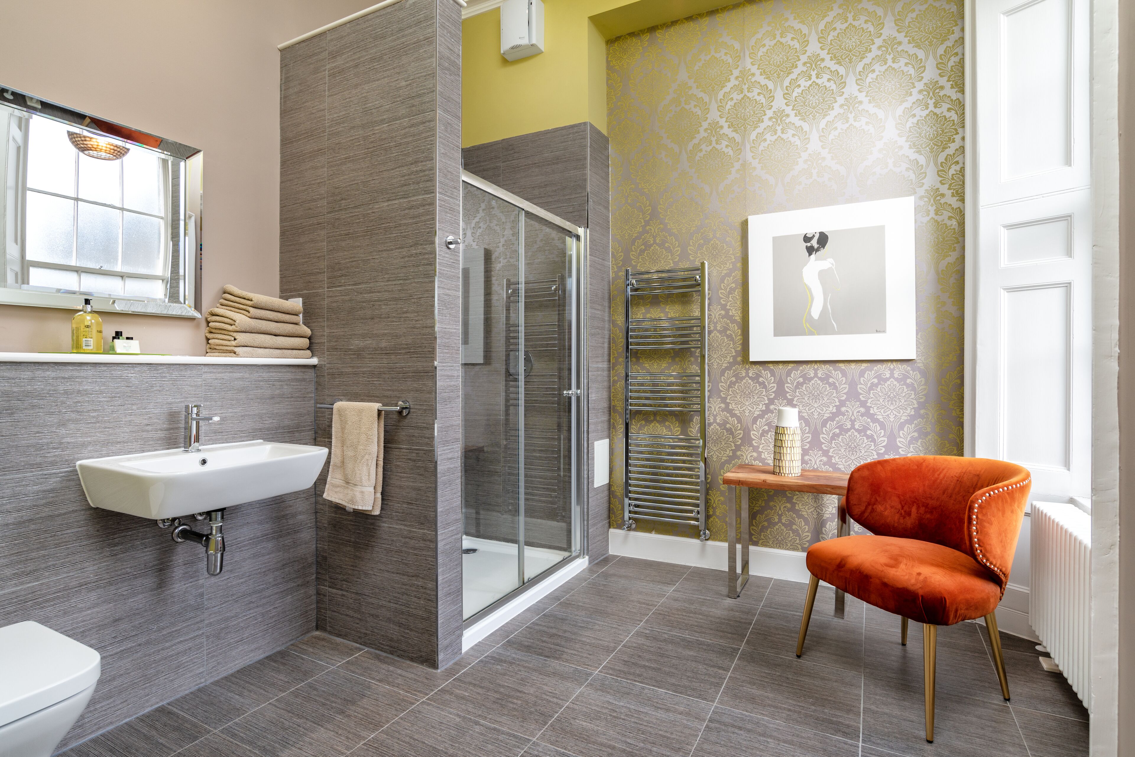 A modern bathroom with a glass shower, a sink, and a chair.