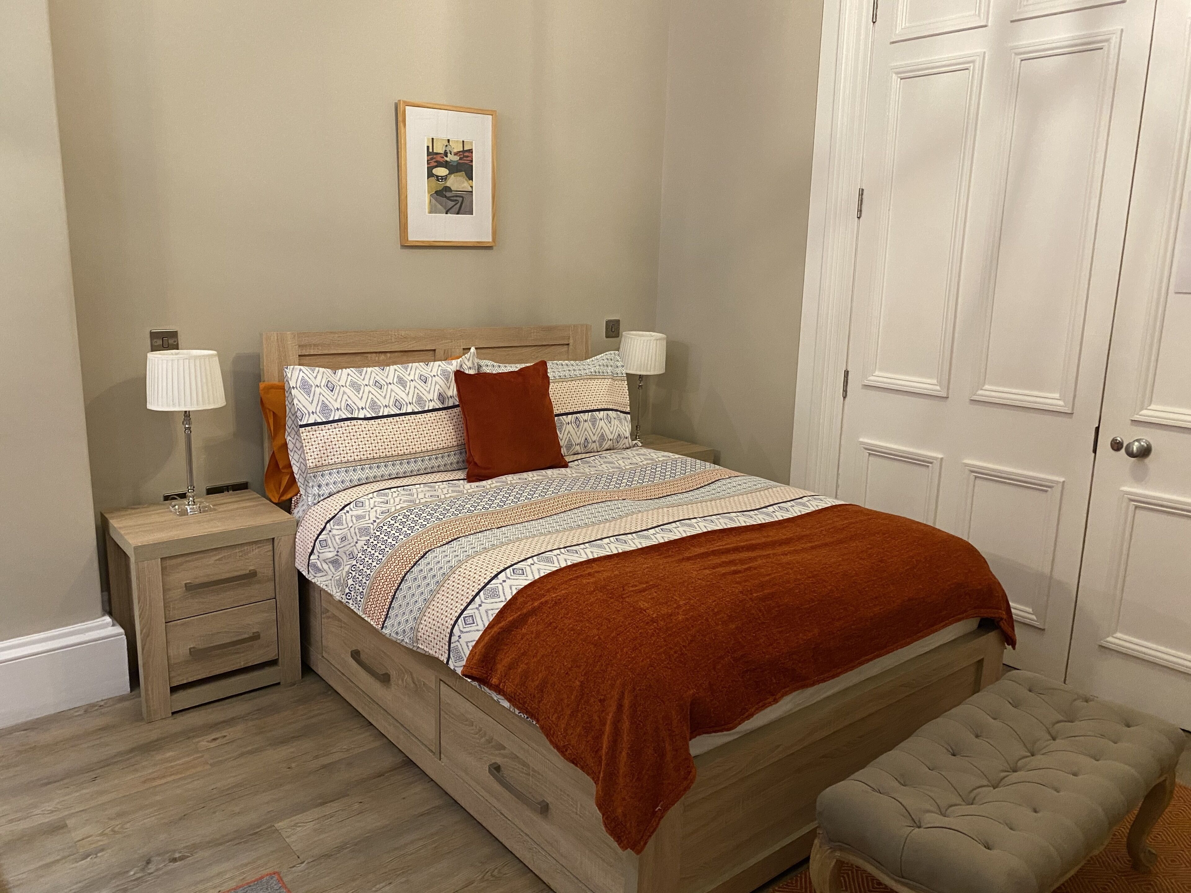 A bedroom with a wooden bed, two bedside tables, a nightstand, a bench, and a door.