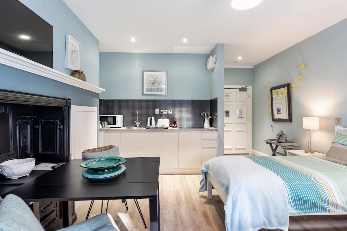 A modern hotel room with a kitchen area, a dining table, and a bed.