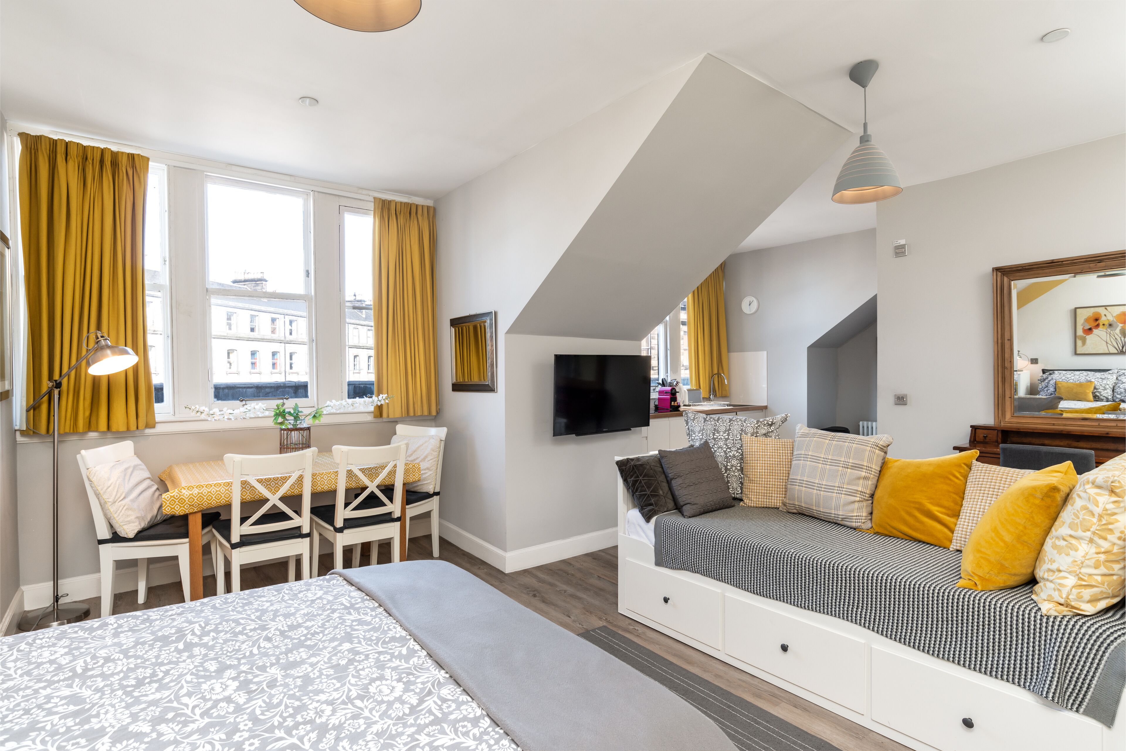 A modern bedroom with a bed, a sofa, a TV, and a dining area with a table and chairs.